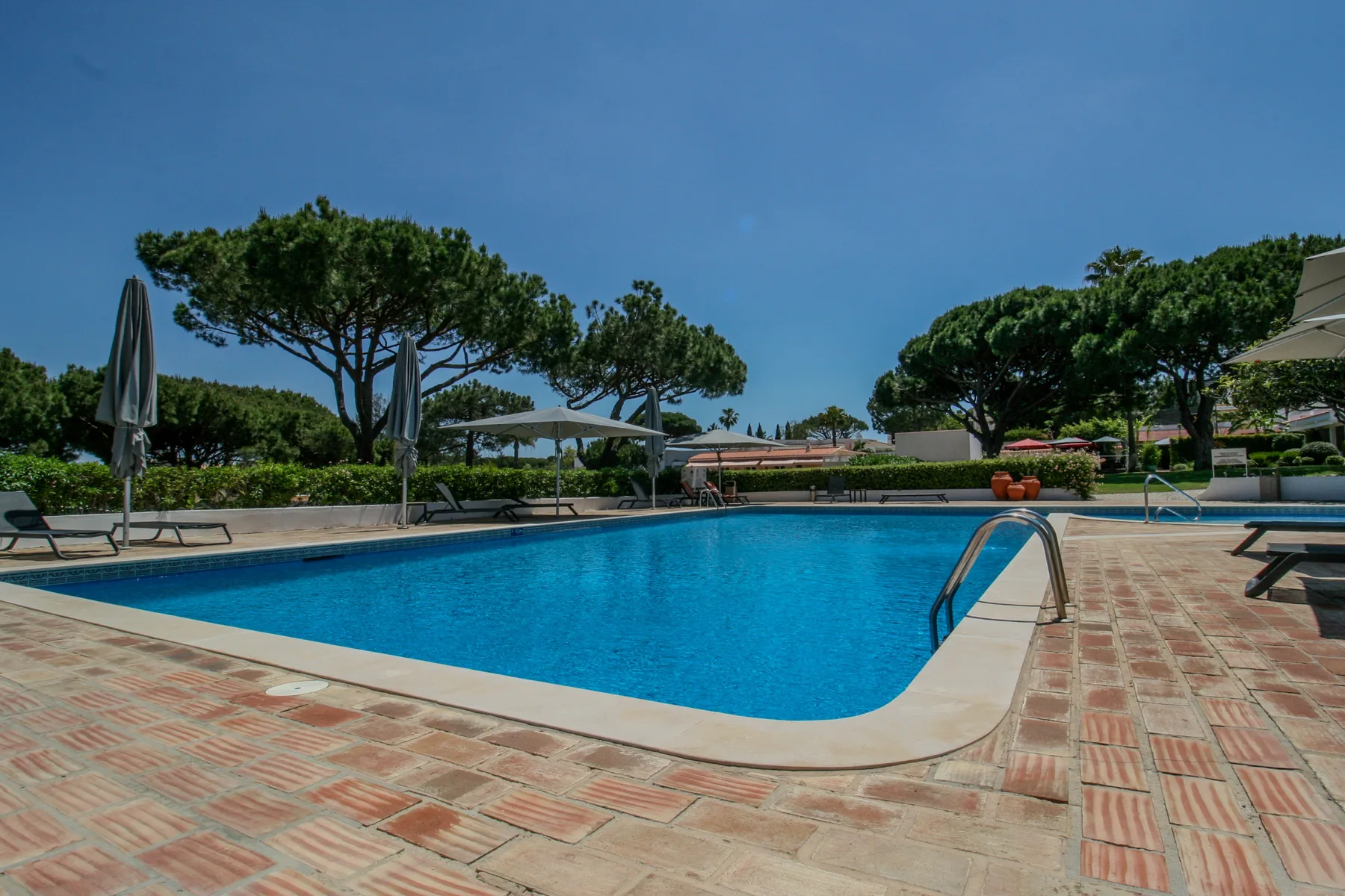Una piscina al aire libre está rodeada por un patio pavimentado y asientos de descanso.