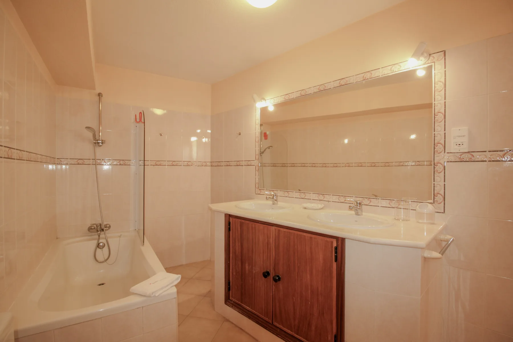 Un baño alicatado con bañera y un amplio lavabo bajo un espejo grande.