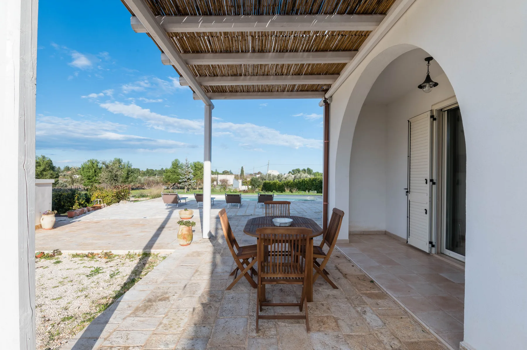 Un patio exterior cubierto con una mesa de comedor de madera y sillas junto a una puerta arqueada.