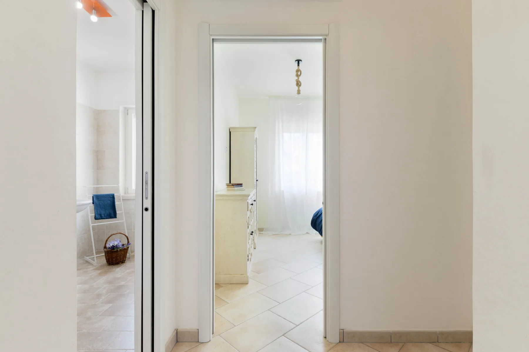 Un pasillo interior luminoso da a una habitación con suelo de baldosas y ventana.