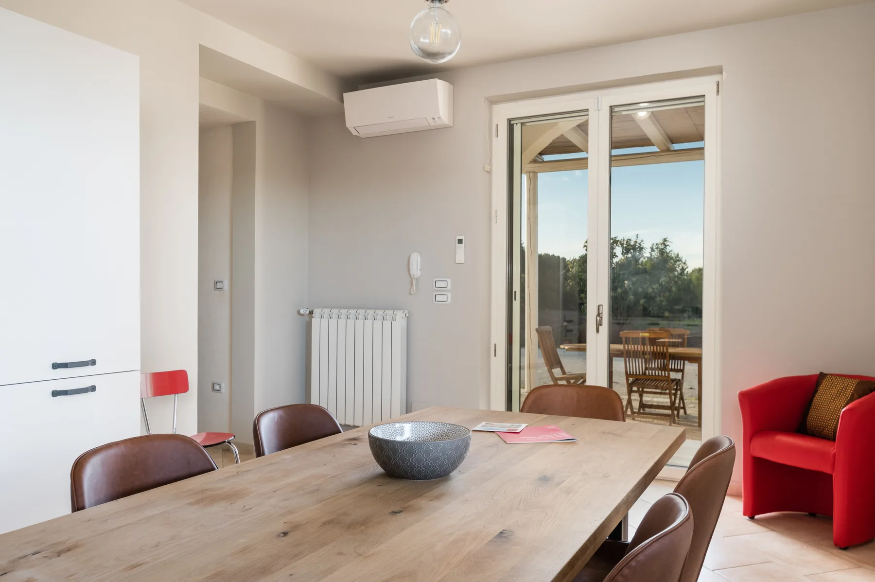 Comedor con mesa de madera, sillas y puertas de cristal que dan a un patio.