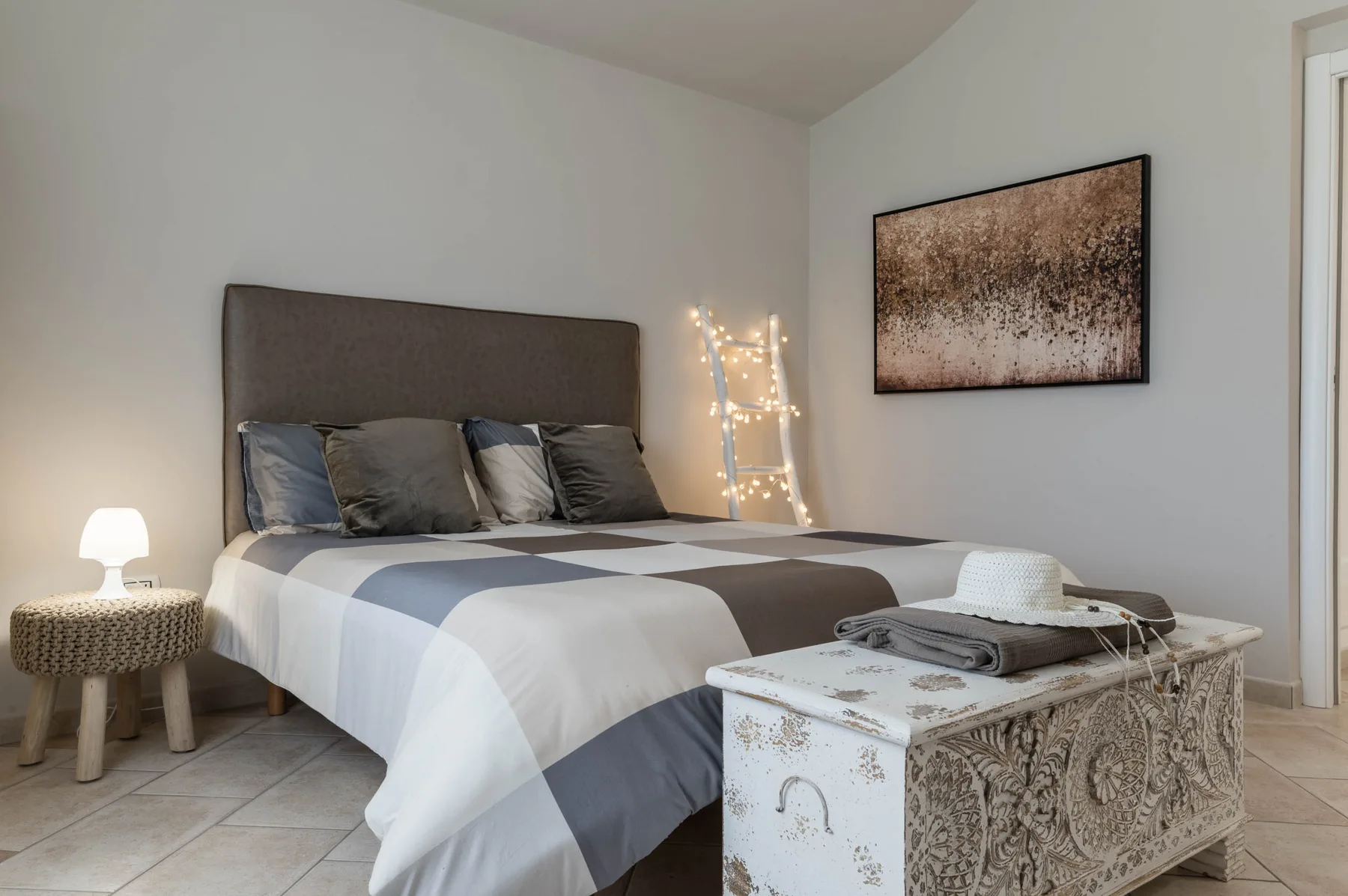 Un dormitorio con una cama bien tendida y un baúl decorativo a los pies.