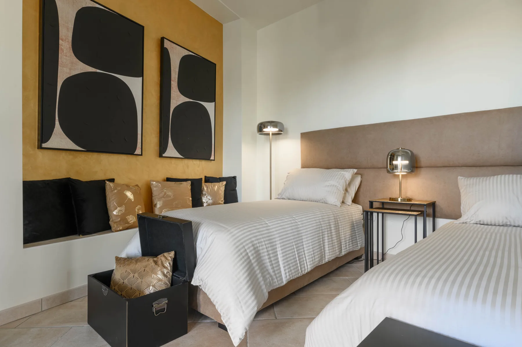 Un dormitorio con dos camas, ropa de cama a rayas y arte abstracto en la pared.