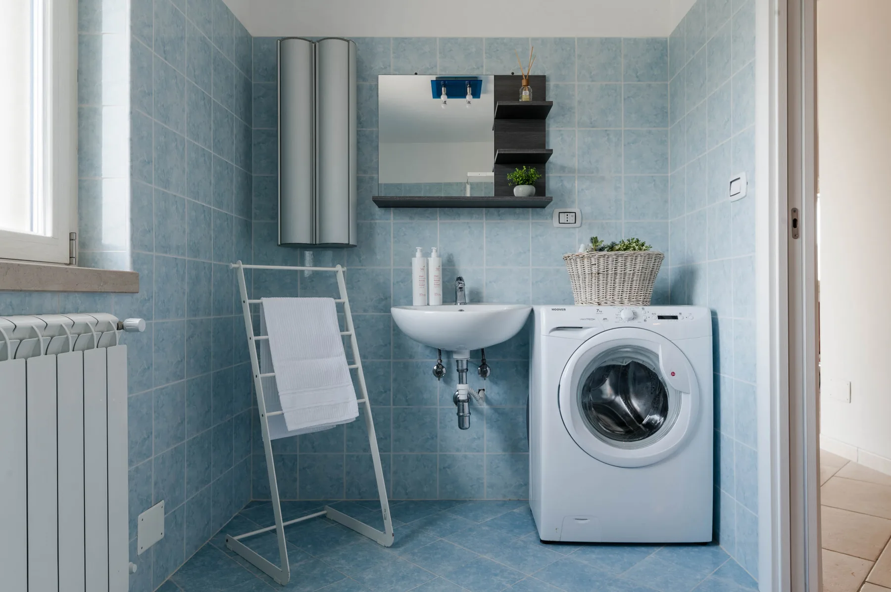 Un baño con azulejos, lavabo, lavadora y toallero.
