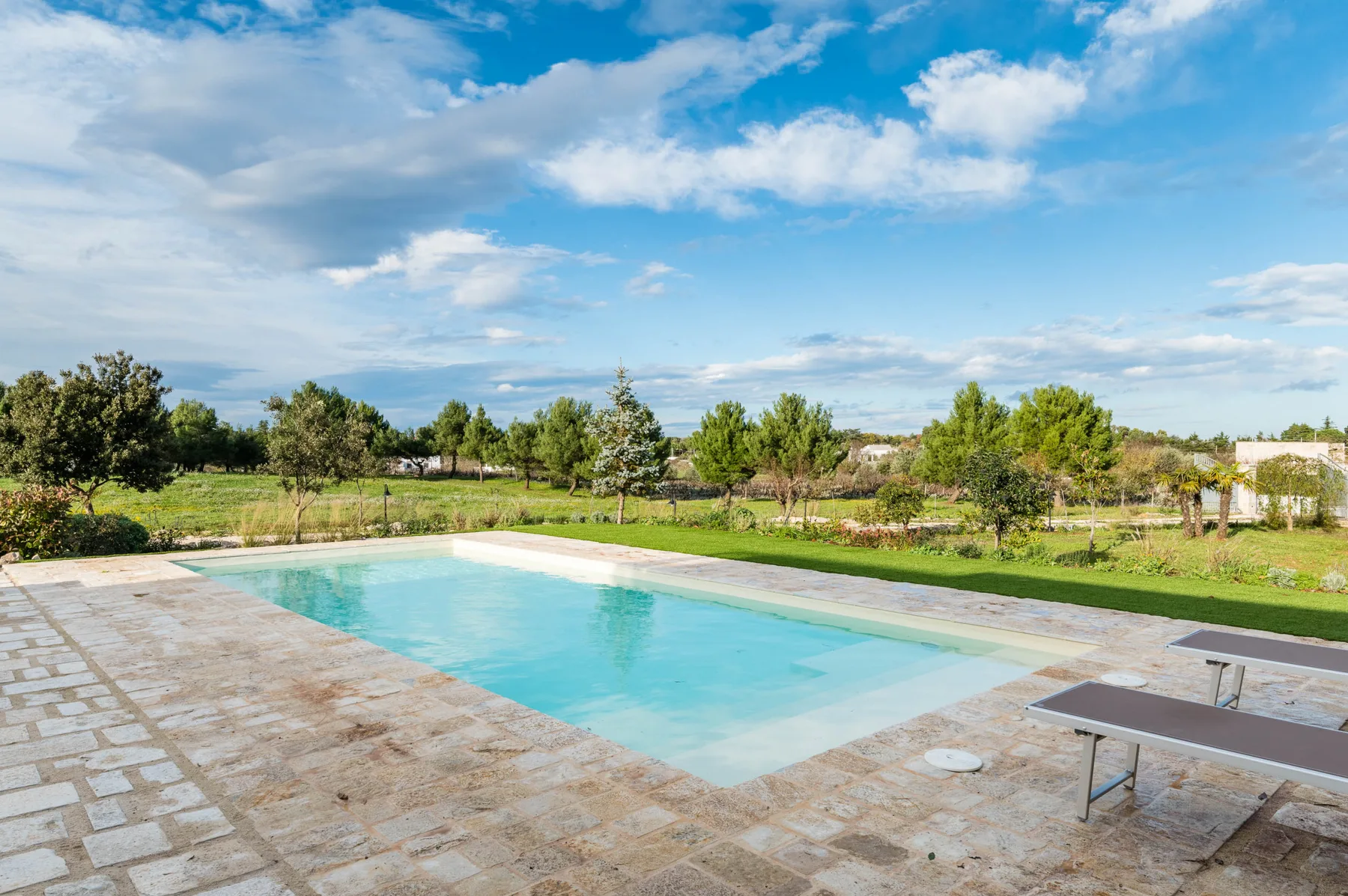 Una piscina al aire libre junto a un patio pavimentado y zonas verdes.