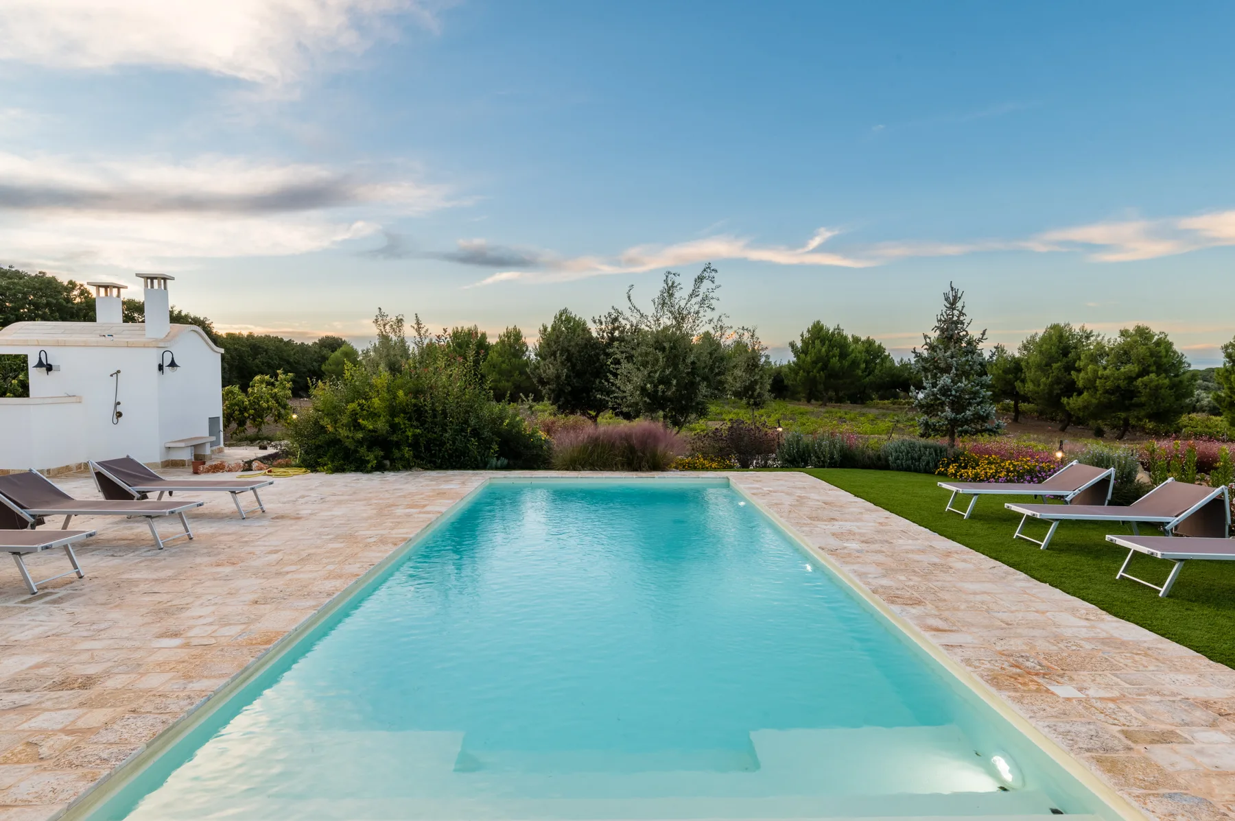 Una piscina al aire libre junto a un patio pavimentado y un jardín.