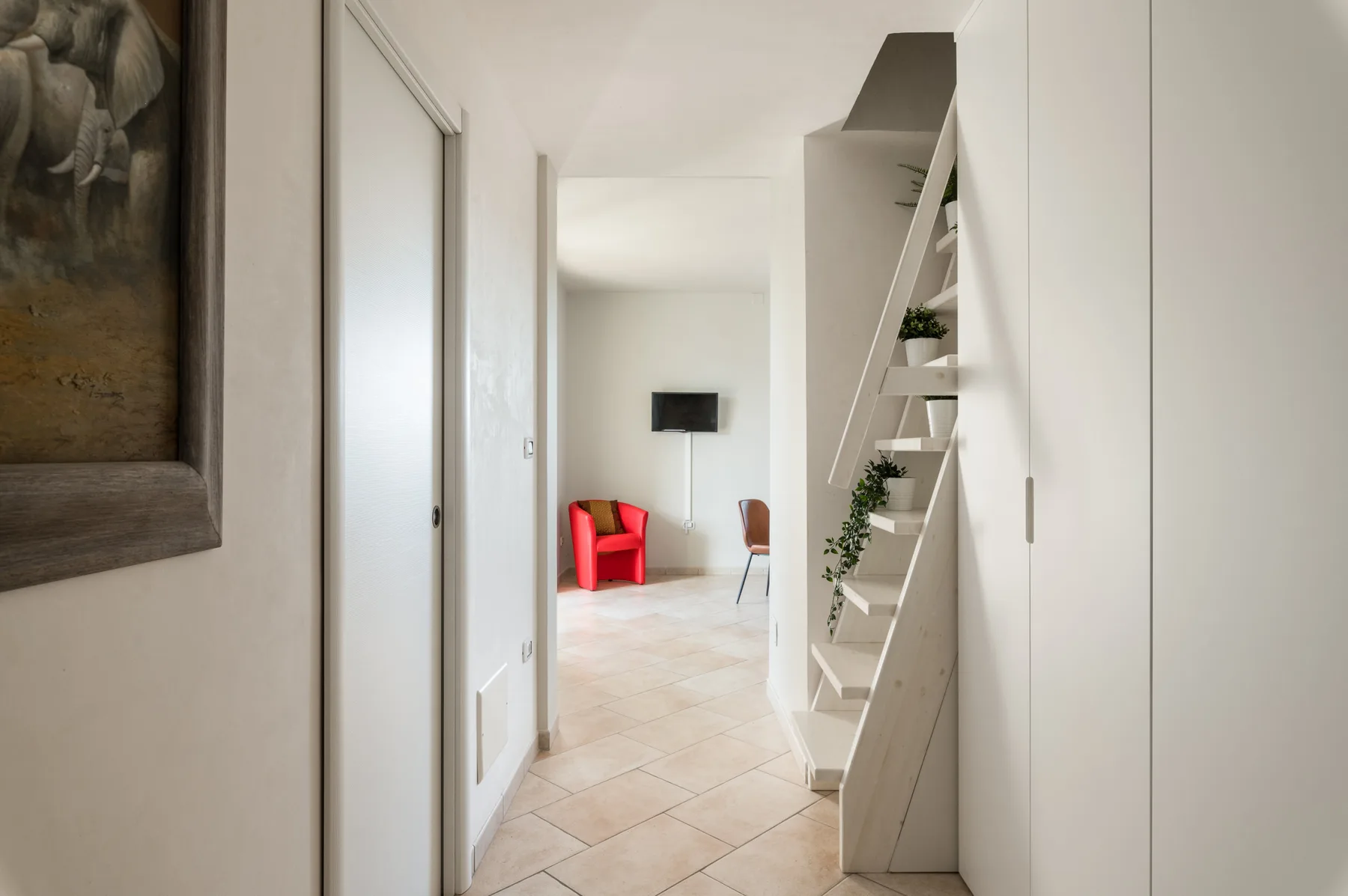 Un pasillo luminoso se abre a una zona de estar con asientos rojos y un televisor en la pared.