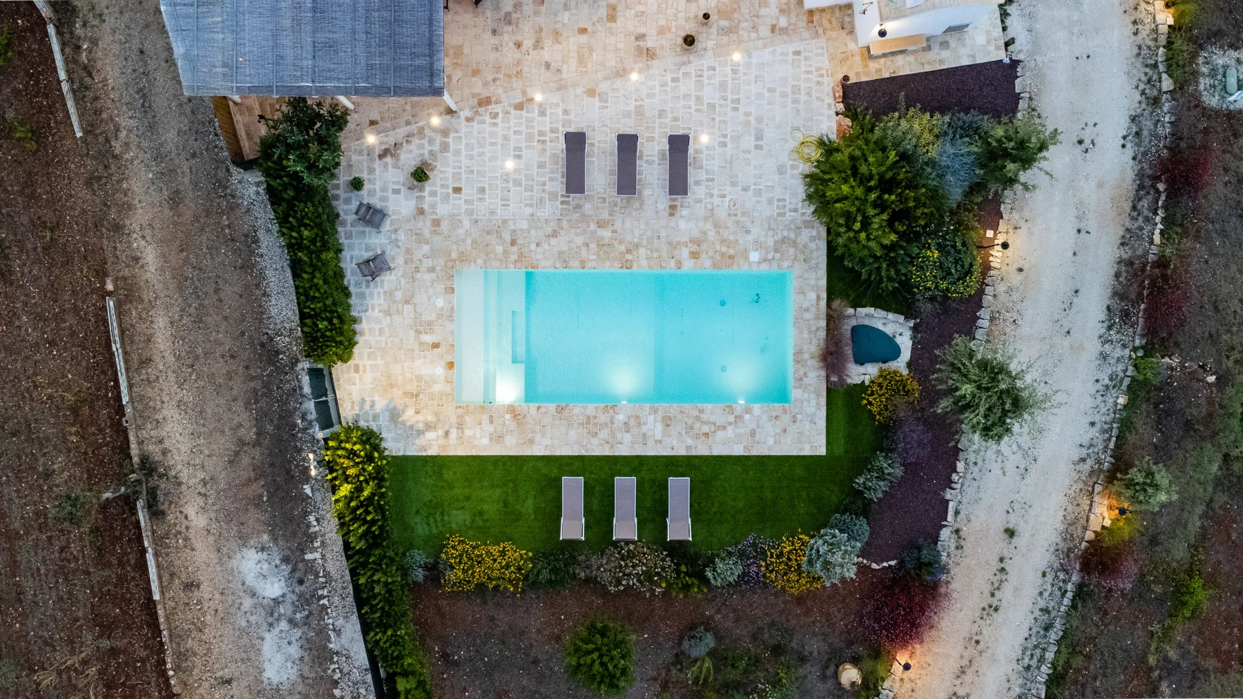 Vista aérea de una piscina rectangular rodeada de pavimento y vegetación.