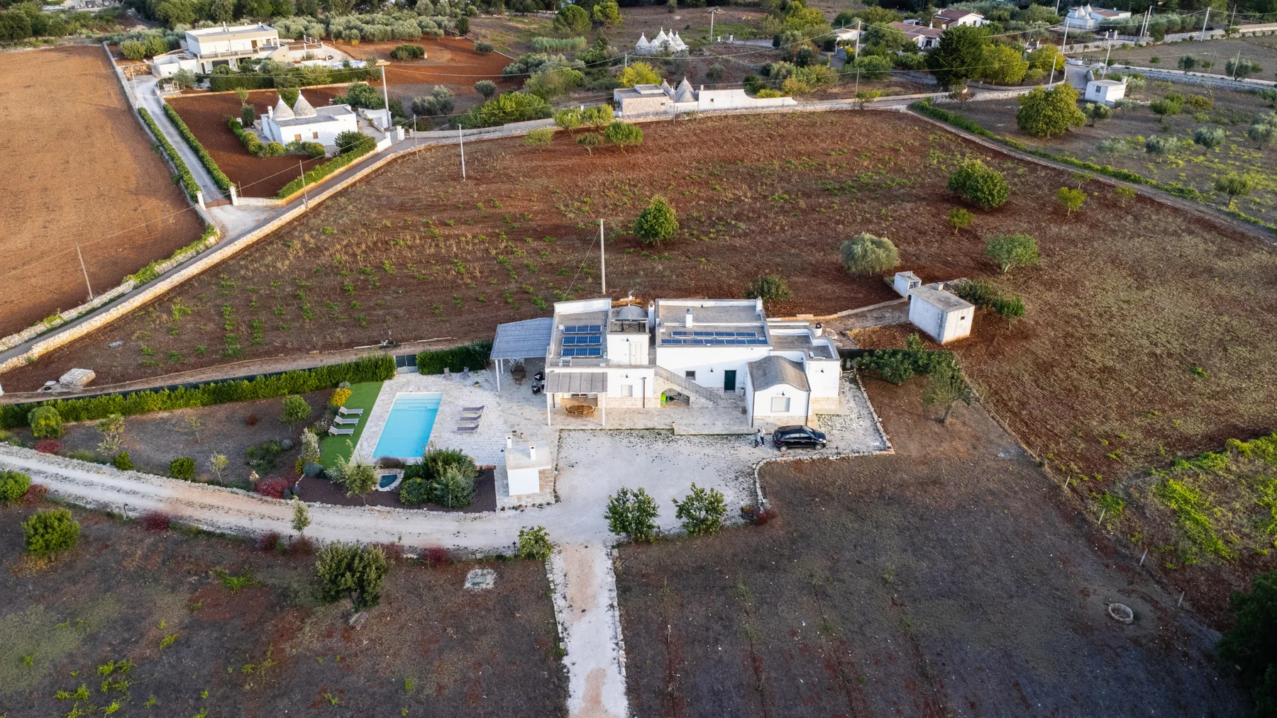 Vista aérea de una propiedad baja rodeada de campos abiertos, con una pequeña piscina cerca.