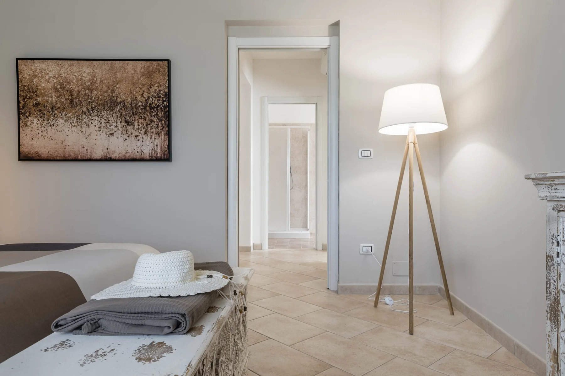 Un dormitorio luminoso con una cama, arte enmarcado y una lámpara de pie junto a una puerta abierta.