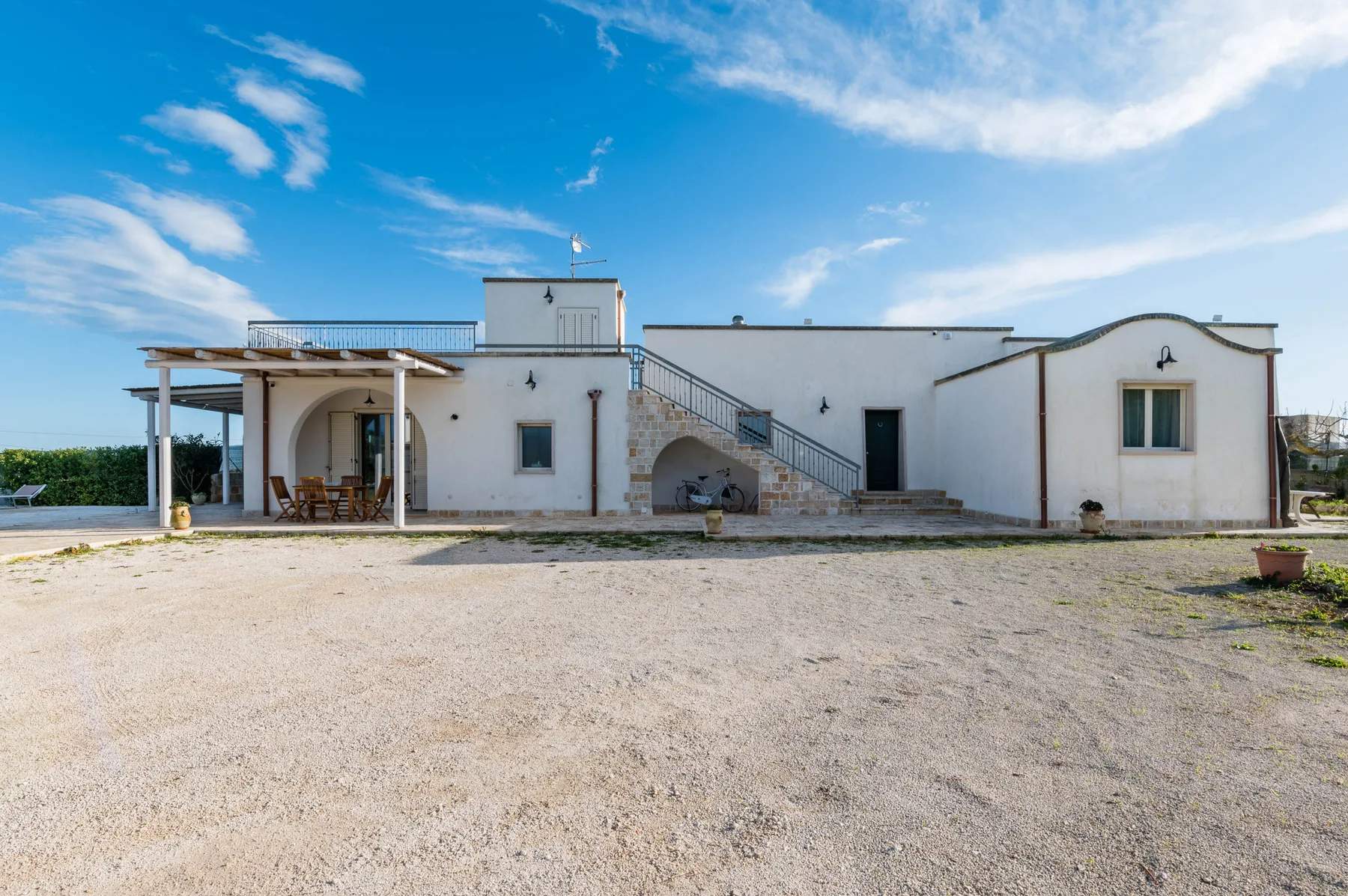 Un edificio blanco con una escalera exterior y un patio cubierto junto a un patio de grava.