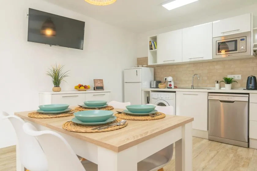 A dining table sits in a bright kitchen with white cabinets and a countertop.