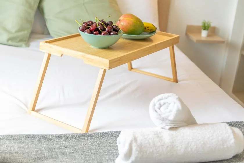 A bed with a wooden breakfast tray holding fruit and folded white towels.