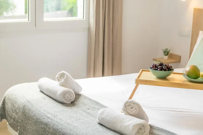 A bright bedroom with a neatly made bed, folded towels, and a tray of fruit.