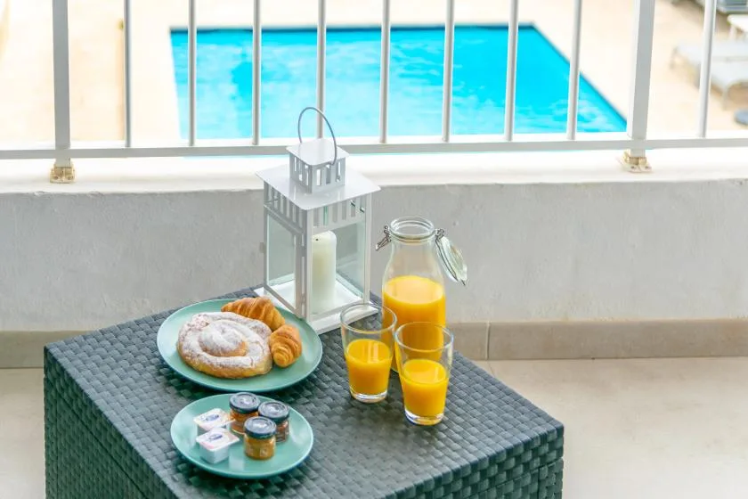 Breakfast with pastries and orange juice sits on a table beside a swimming pool.