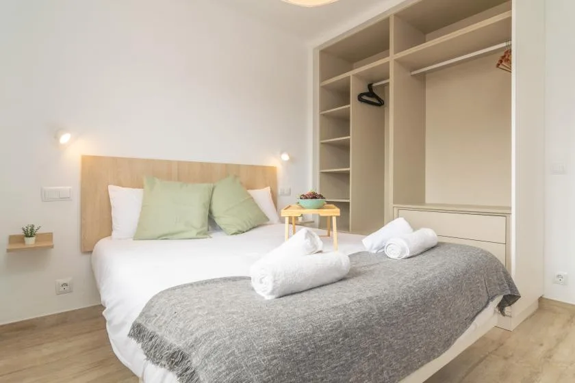 A bedroom with a neatly made bed and an open built-in wardrobe.
