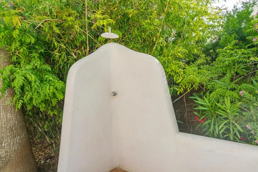 An outdoor shower area with a curved white wall surrounded by greenery.
