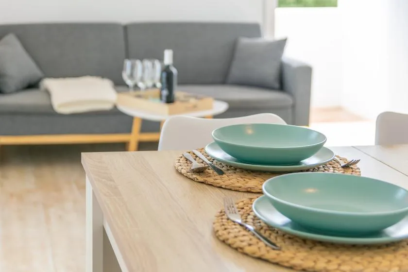 A dining table set with green dishes sits in front of a living room seating area.