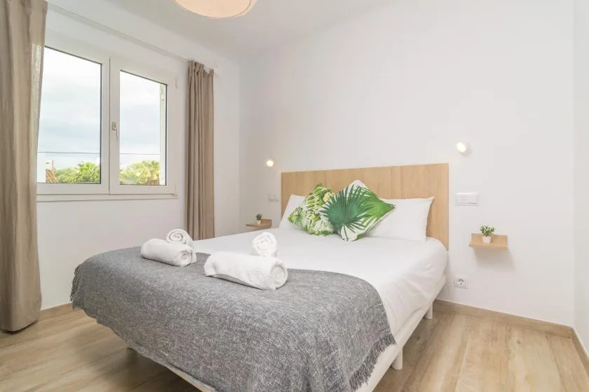 A bright bedroom with a bed dressed in white and a leafy accent pillow.