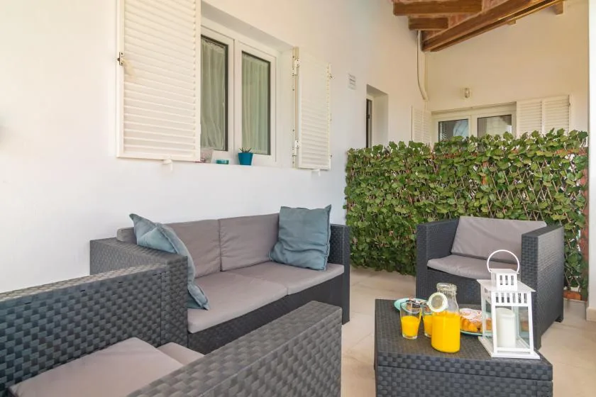 Una zona de estar en un patio cubierto, con muebles acolchados y un seto frondoso.