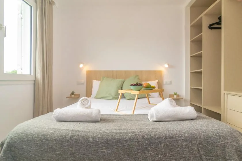 A bedroom with a bed, folded towels, and a small table holding fruit.