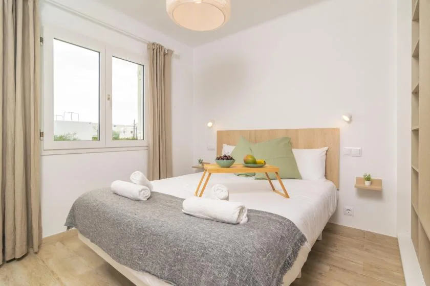 A bright bedroom with a bed, bedside lights, and a large window.