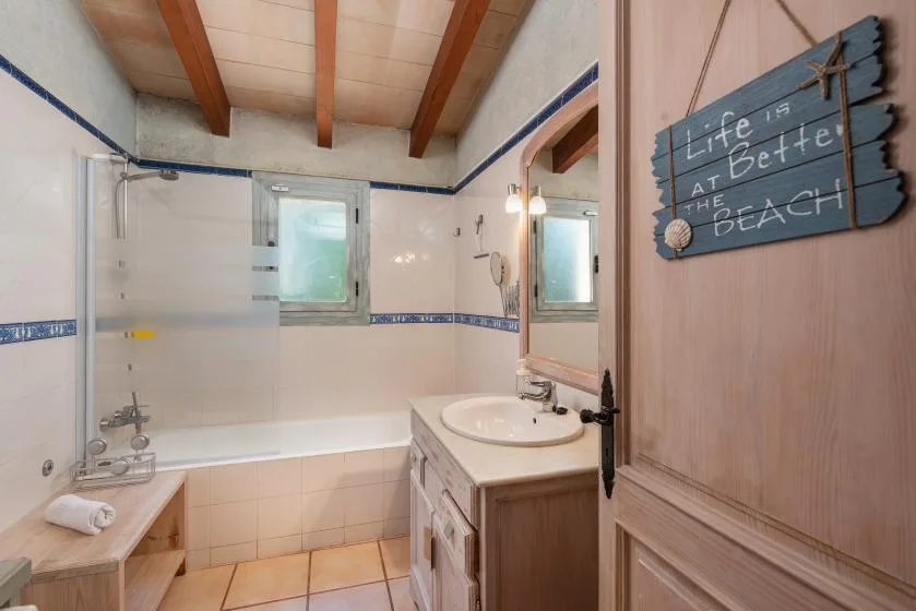 A tiled bathroom with a bathtub, vanity, and wooden ceiling beams.