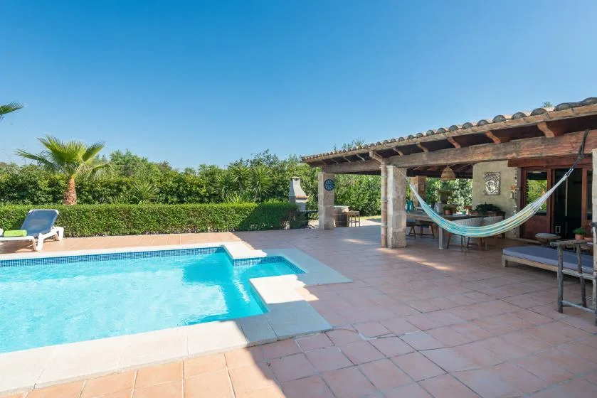 Una piscina al aire libre junto a un patio sombreado con una hamaca.