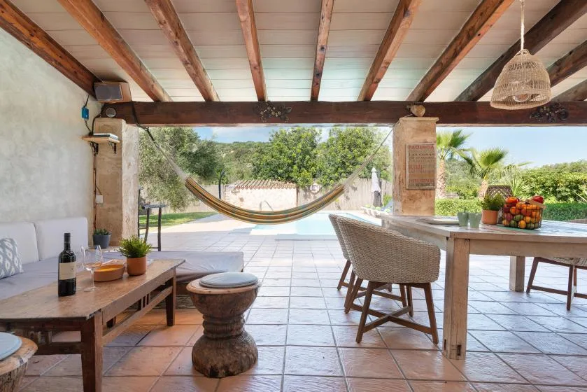 Un patio cubierto con mesa de comedor, asientos y una hamaca frente a un jardín.