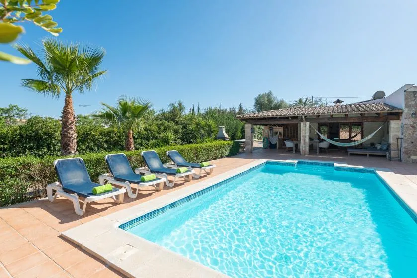 Una piscina al aire libre junto a asientos, palmeras y un patio cubierto.