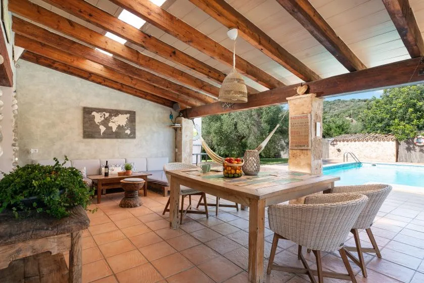 A covered outdoor dining area with a wooden table and a hammock in the background.