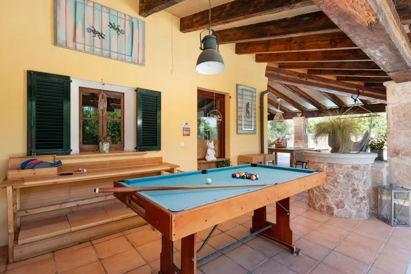 A pool table sits in a covered patio area with exposed wooden beams.
