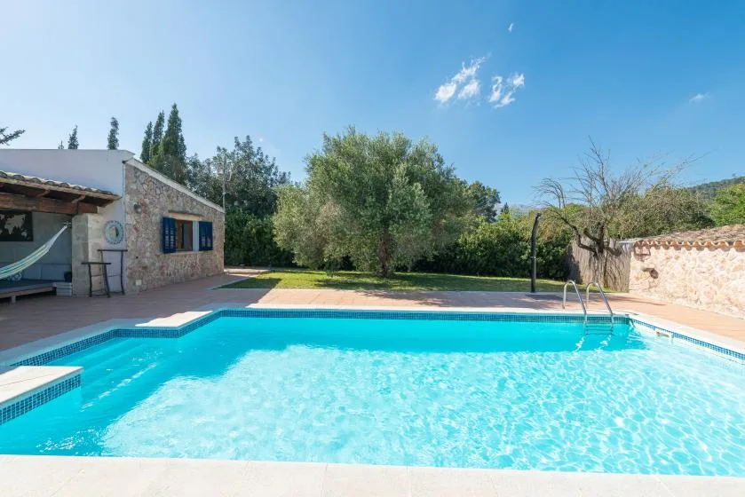 An outdoor swimming pool beside a stone building and leafy garden.