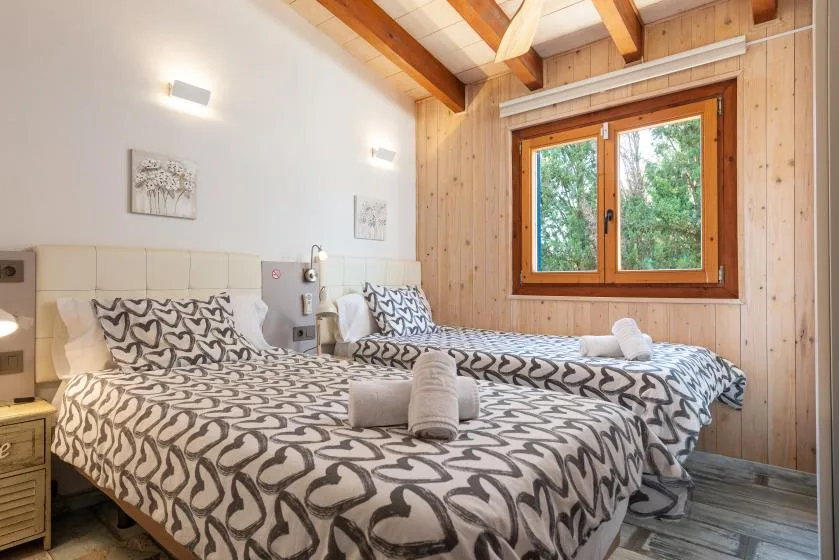 A bedroom with two beds, patterned bedding, and a large wooden-framed window.