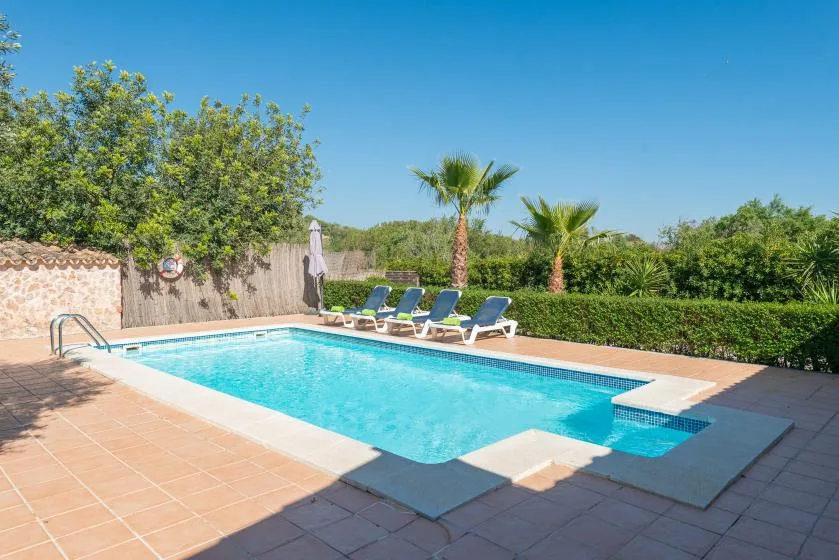 An outdoor swimming pool is surrounded by tiled paving and lounge seating.