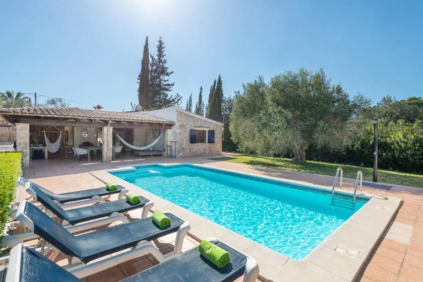 A swimming pool beside a shaded patio, with loungers along the water.