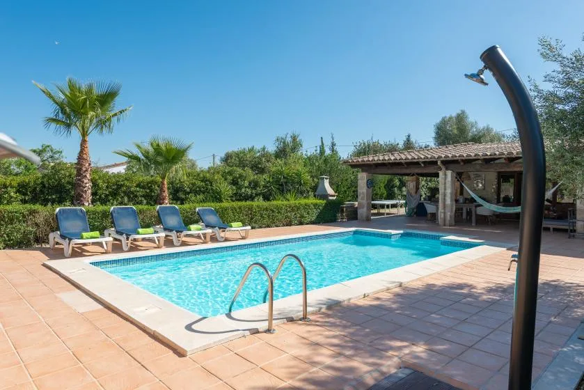 An outdoor swimming pool sits beside a shaded patio with lounge seating.