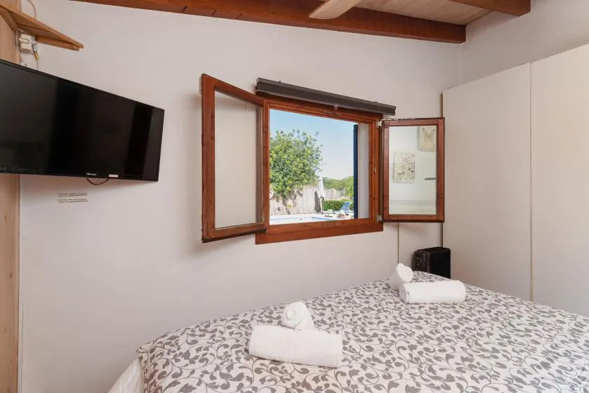A bedroom with patterned bedding and an open window overlooking greenery.