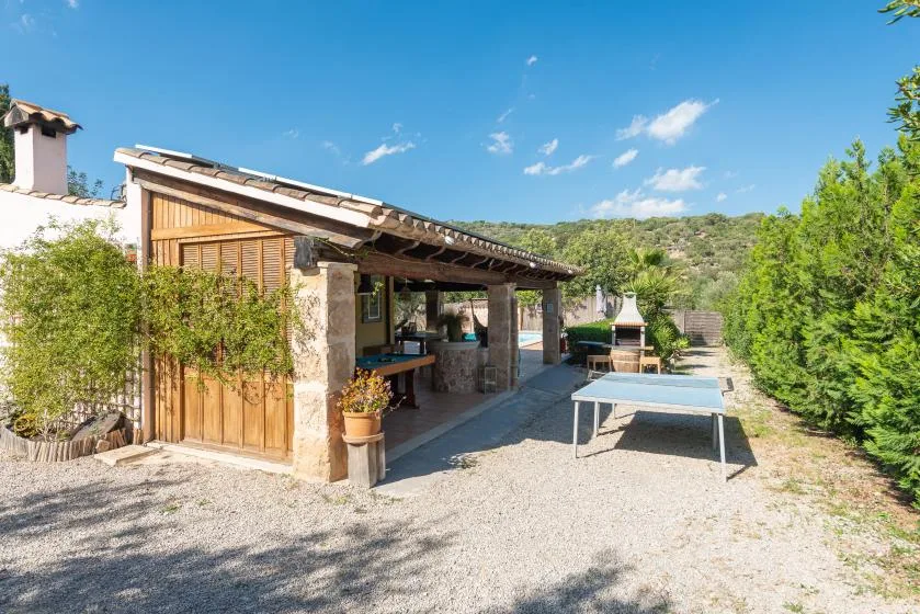 A covered outdoor patio with a table and seating beside a rustic building.