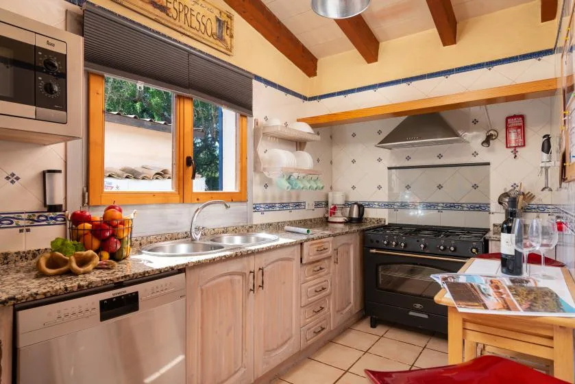 A kitchen with wooden cabinets, a sink, and a stove beneath exposed ceiling beams.