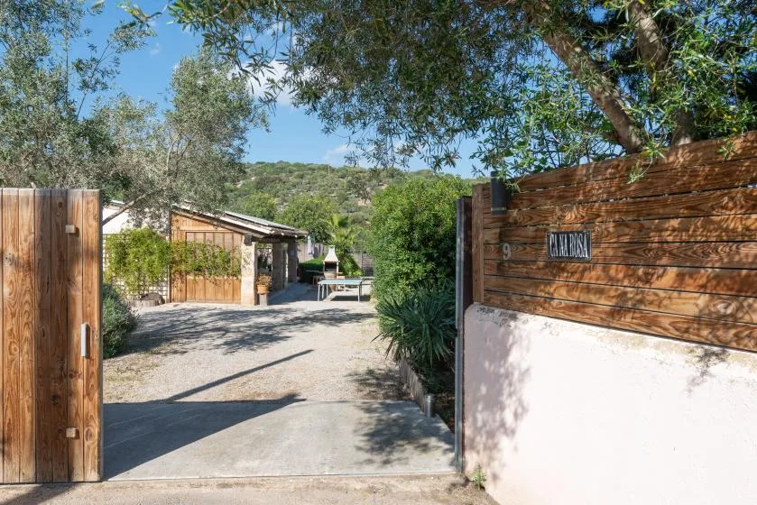 An open wooden gate leads into a gravel courtyard with trees and a small building.
