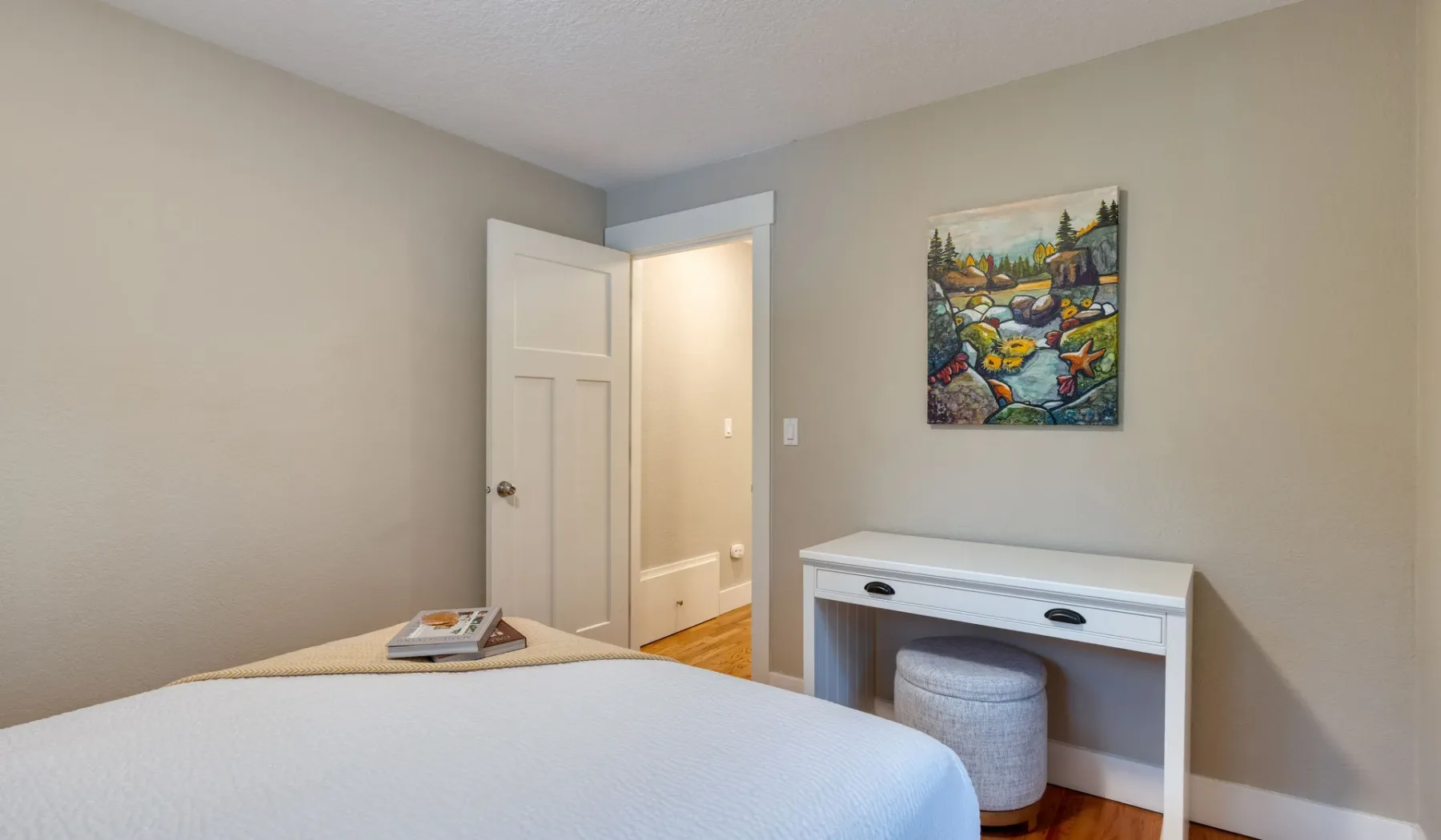 Dormitorio con una cama, un escritorio blanco y arte colorido en la pared.