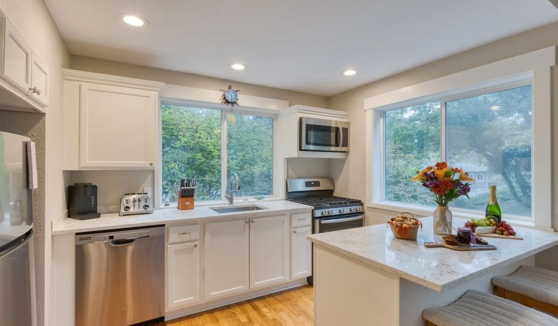 Una cocina luminosa con gabinetes blancos, ventanas grandes y una isla central.