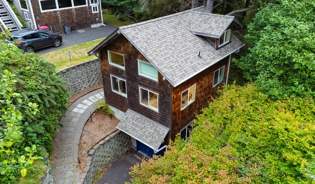 Una casa marrón con techo gris se encuentra entre árboles verdes densos.
