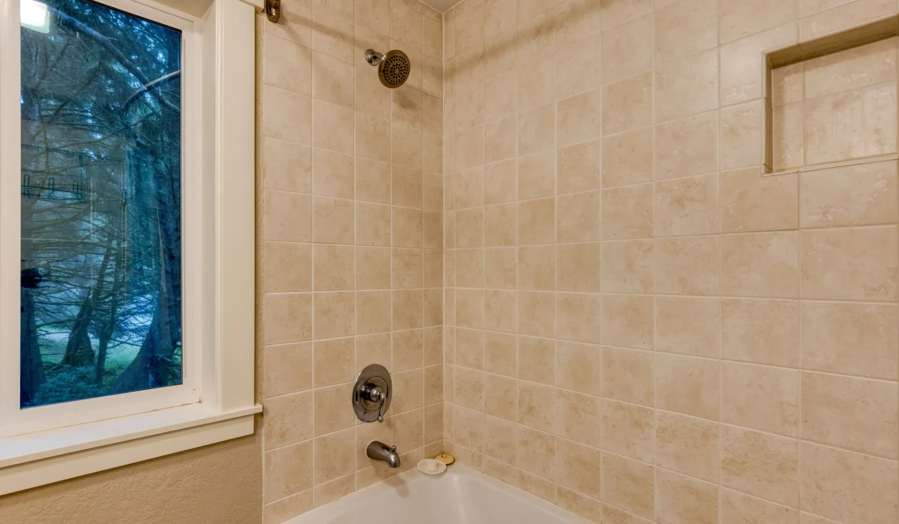 Zona de ducha de baño con azulejos junto a una ventana.
