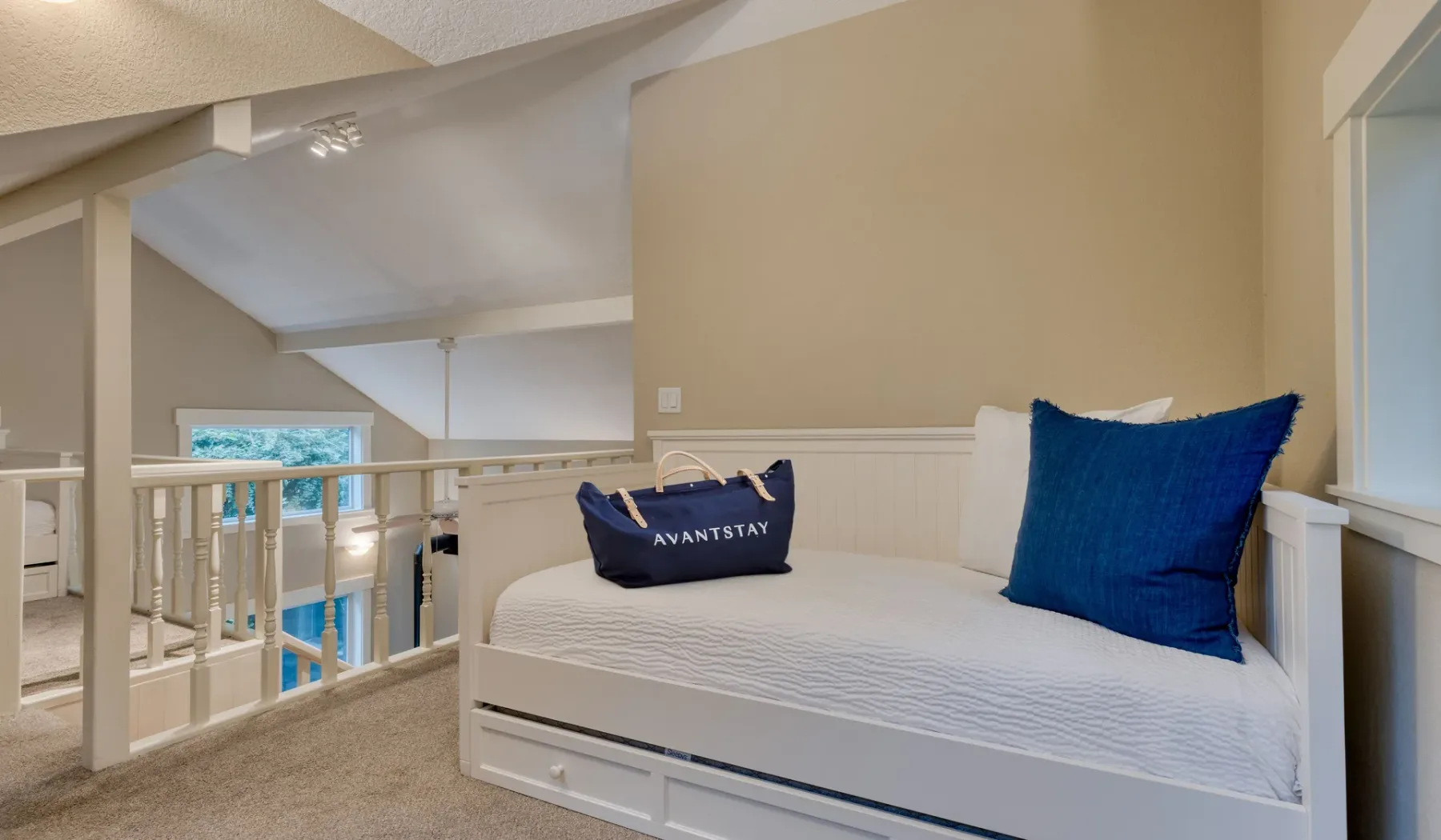 Una cama con almohadas azules está junto a una barandilla blanca en una habitación alfombrada.