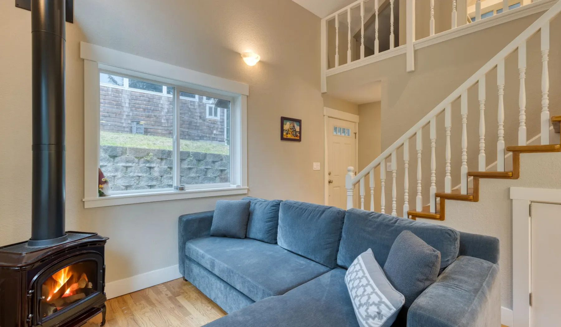 Sala de estar con asientos azules junto a una escalera y una ventana grande.