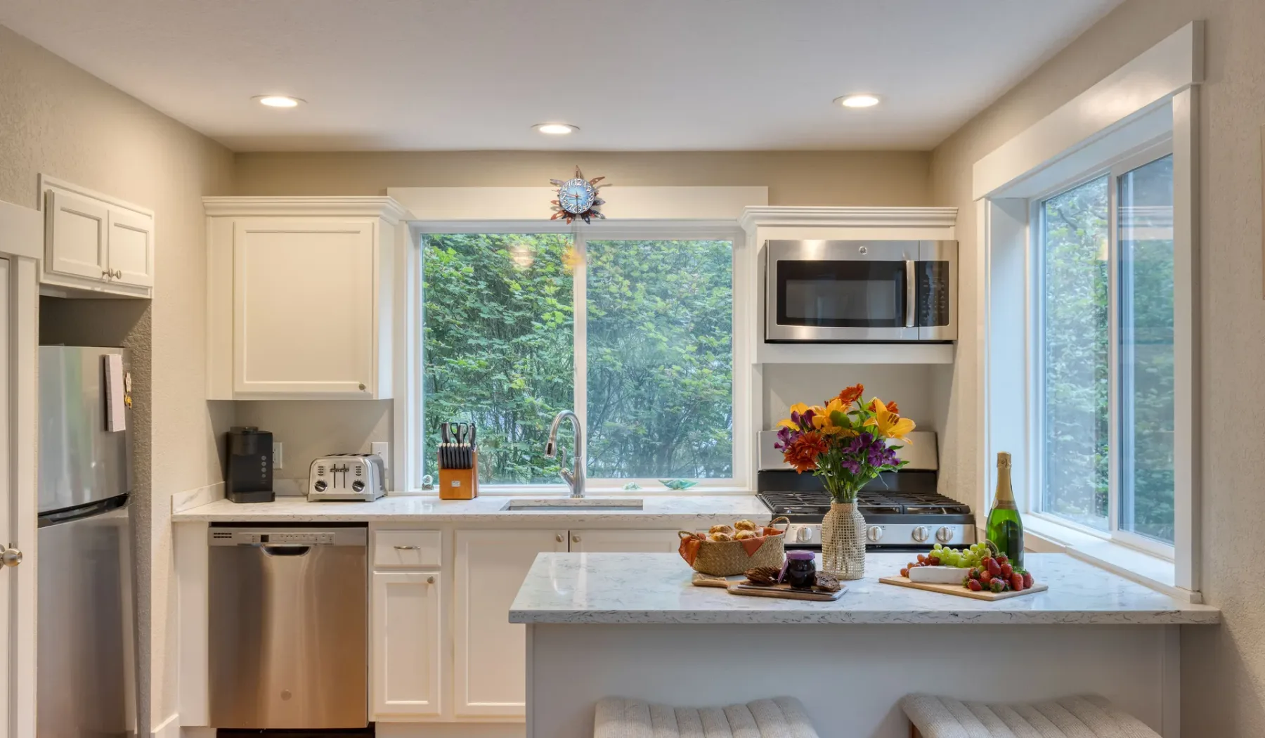 A bright kitchen with white cabinetry, wide windows, and a central island.