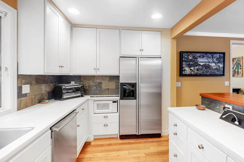 A bright kitchen with white cabinetry, stainless steel appliances, and wood flooring.