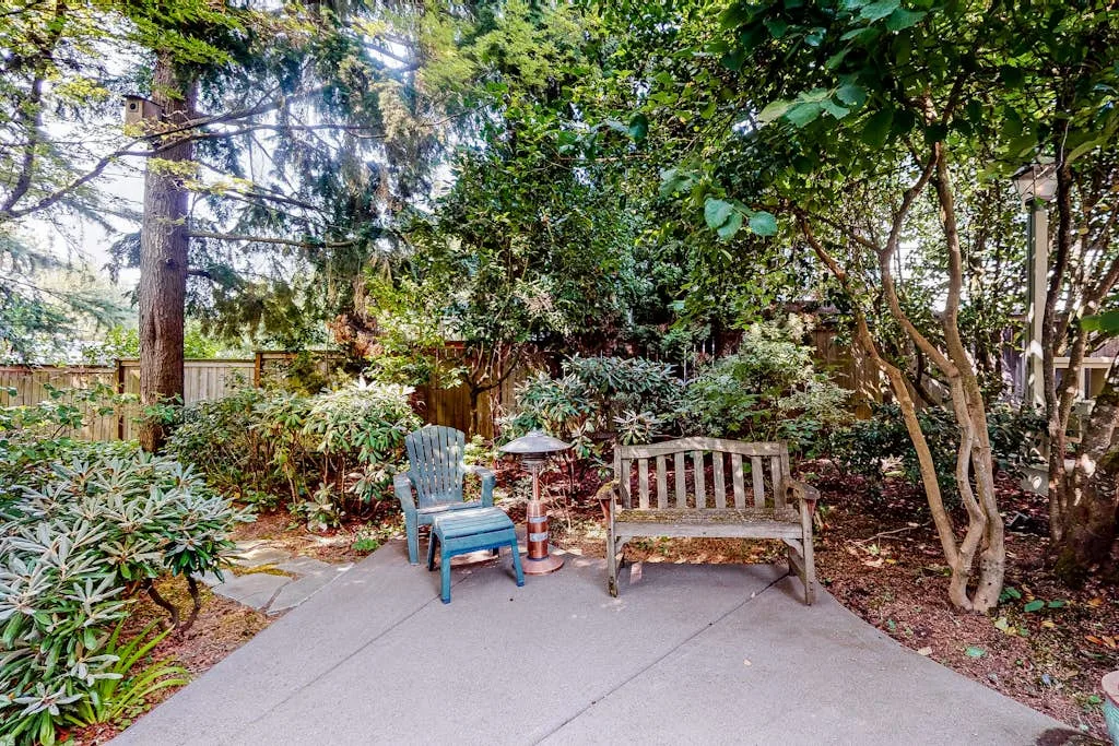 A garden patio with outdoor seating surrounded by trees and shrubs.